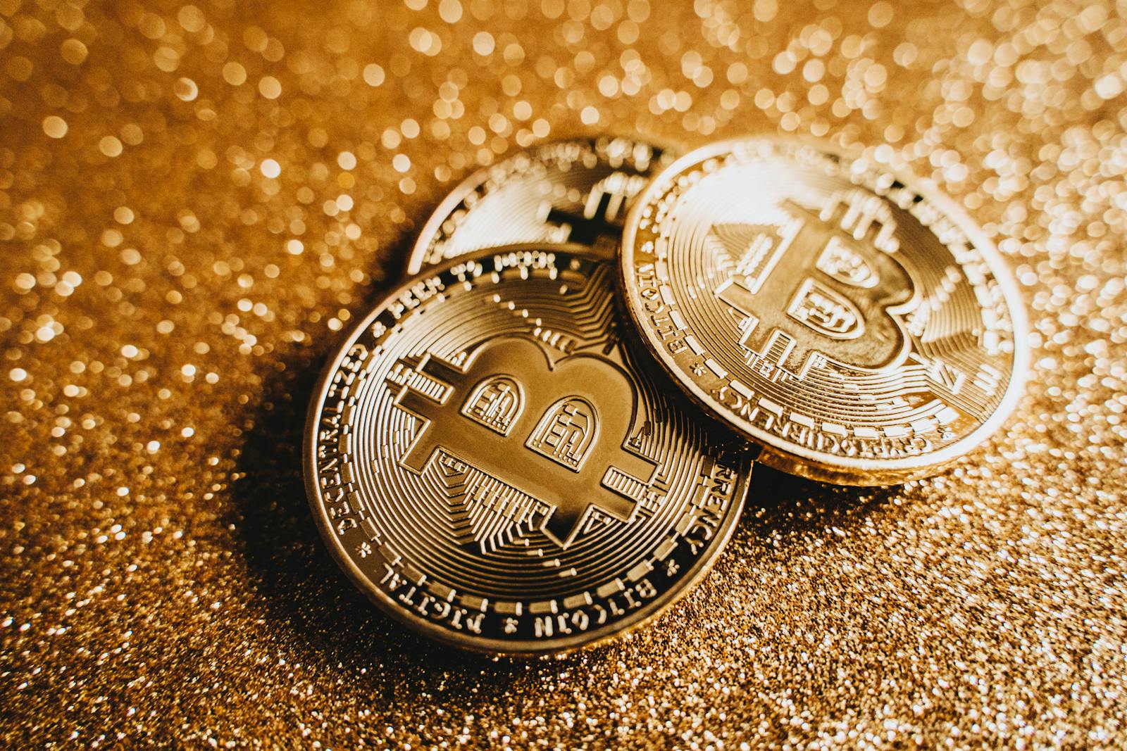 Close-up of shiny bitcoins on a gold glitter background, symbolizing cryptocurrency wealth.